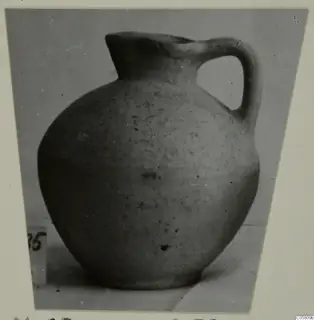 Pottery jug with a single loop handle and a globular body, photographed on a plain surface.