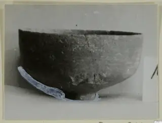 Pottery bowl with an uneven rim and a long crack down its side, seen from the side