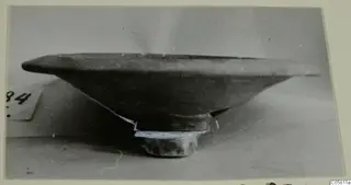Pottery bowl with a wide flat rim and short foot, seen from the side beside a number label