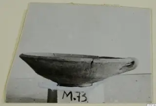 Pottery Red Slip bowl in side view, standing on a small stand with a number label