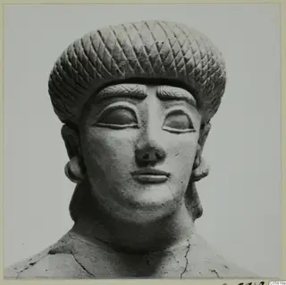 Terracotta head and shoulders of a figure with a diamond-patterned headdress and heavy-lidded eyes