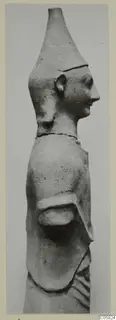 Terracotta statuette of a figure in side profile facing right, with a tall conical headdress and one arm bent at the waist