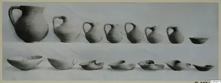 Row of handled jugs and a row of bowls, pottery from Tomb 1 at Idalion, laid out on a pale cloth.