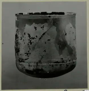 Blown glass vessel from Idalion, straight-sided with a rounded base, its surface pale and dark patched from weathering