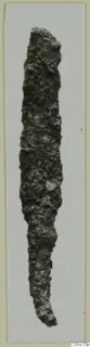 Iron weapon, long and narrow with a heavily corroded surface, photographed upright on a pale background
