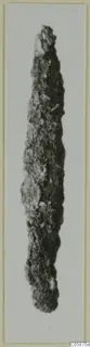 Corroded iron object, long and narrow, tapering to a point at the top, photographed on a pale background
