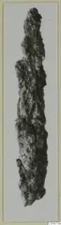 Corroded iron weapon, long and narrow, photographed against a pale background.
