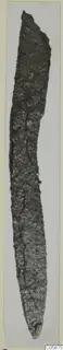 Corroded iron knife with a long, narrow, slightly curved blade, photographed upright