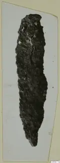 Corroded iron tool, long and narrow, tapering to a point at its lower end.