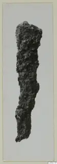 Iron Bronze Age knife, heavily corroded and crusted, photographed upright against a pale background.