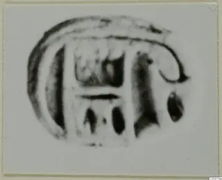 Blurred enlarged photograph of an engraved glyptic object, probably a seal or gem, with a curved outline and rectangular motifs.