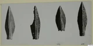 Four pointed, leaf-shaped metal blades laid in a row on a pale grey surface, Idalion finds.