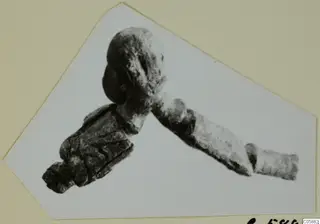 Bronze fibula photographed on a cut card mount, with a rounded head and a long bow extending diagonally