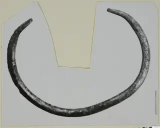 Open bronze bracelet with tapering ends, lying flat and photographed on a pale card mount.