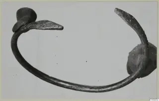 Bronze bracelet with an open ring and flattened, tapering terminals, photographed on a pale background.