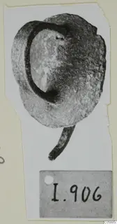 Bronze fragment with a curved loop and a short rod-like projection, photographed on a card with a number label