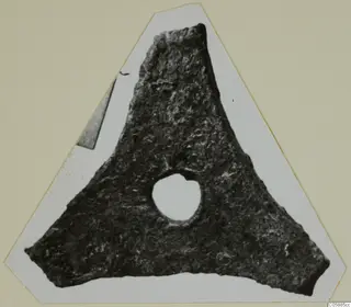 Triangular bronze fragment with a round hole near its centre, shown cut out and mounted on a card