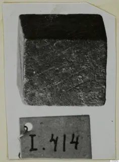 Cube-shaped bronze weight, dark and corroded, shown with its number label.