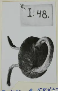 Corroded metal mounting with a loop and two bent prongs, photographed on a card with a number label