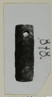 Cylindrical dark metal fragment with a round hole near one end, photographed on a mounted card.