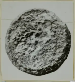 Round lead object, heavily corroded, photographed face-on against a pale background.