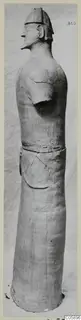 Terracotta standing figure with a helmet-like headdress, shown in profile facing left