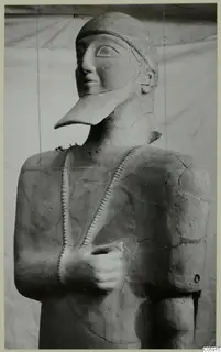 Terracotta Neo-Cypriote statue of a standing figure with a pointed beard and cap, one hand held against the chest.