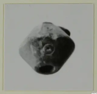 Blurred photograph of a small faceted object with a ringed circular motif on one face, a small find from Idalion