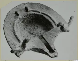 Lamp with a shallow round basin, a long projecting nozzle at right and a curved lug at lower left, seen from above.