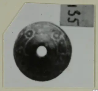 Disc-shaped ornament with a large central hole and raised ring motifs, photographed on white card