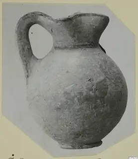 Round-bodied jug with a strap handle and flared mouth, shown on a pale card mount with cut corners