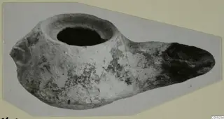 Clay oil lamp with a round filling hole at the top and an elongated nozzle to the right.