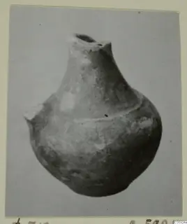Globular pottery vessel with a short neck and broken rim, photographed against a plain grey background
