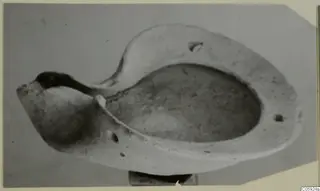 Terracotta lamp with an oval basin, raised rim and pinched spout, photographed against a grey background.