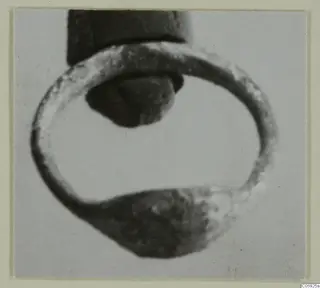 Close-up of a silver ring with a flattened, broader section at the bottom and a dark object inside its loop.