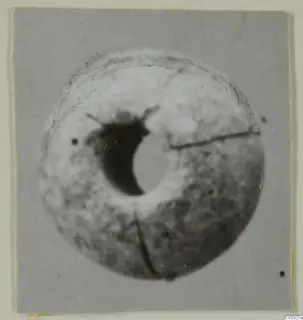 Round bead with a large central hole and cracks across its surface, shown on a grey card