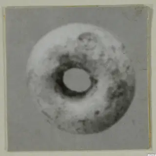 Blurred photograph of a round disc-shaped object with a large central hole, mounted on a grey card