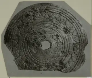Bone disc with concentric grooves and arc patterns around its edge and a central hole