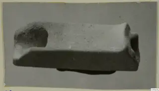 Faience spout, a small rectangular object shown in side view with a hollow opening at one end.