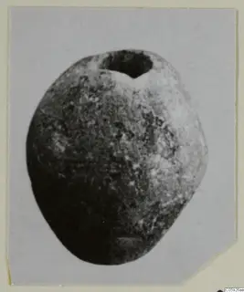 Rounded, pitted stone object with a large hole at the top, shown in close view on a photographic card mount