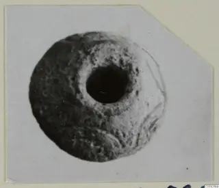 Round object with a large central hole and pitted surface, from Idalion, shown on a mounted card