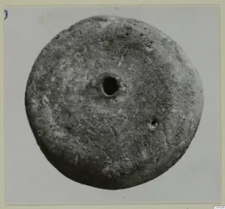 Round disc-shaped small find with a large central hole, photographed against a pale background