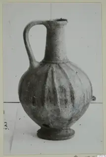 Wheel-made bucchero jug with a single handle, tall neck and vertical ribbing, photographed against a plain background.