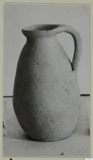 Plain white pottery jug with a single handle, photographed on a pale surface