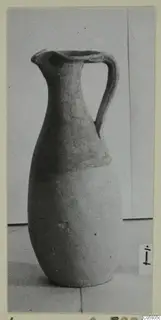 Pottery jug with a single strap handle and pinched spout, photographed on a plain surface