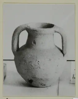 Plain pale pottery jug with two handles and a wide mouth, photographed on a light surface.