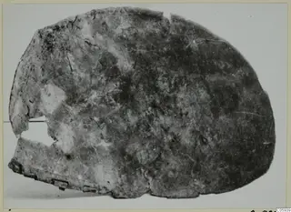 Corroded bronze fragment from Idalion, rounded with broken edges and a hole on the left side