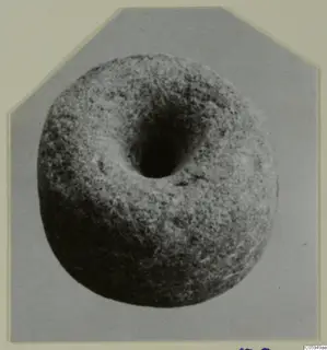 Round object with a large central hole, shown in a photograph mounted on a card