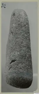Elongated stone object with a rounded top and wider base, photographed upright on a grey backdrop.