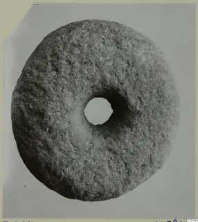 Round stone disc with a central hole, photographed from above on a grey backdrop
